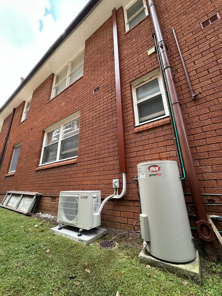 Outdoor air conditioning installation and pipework on the exterior of a red brick apartment building