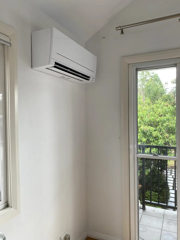 White wall-mounted indoor split system air conditioning unit installed beside a window in a residential room