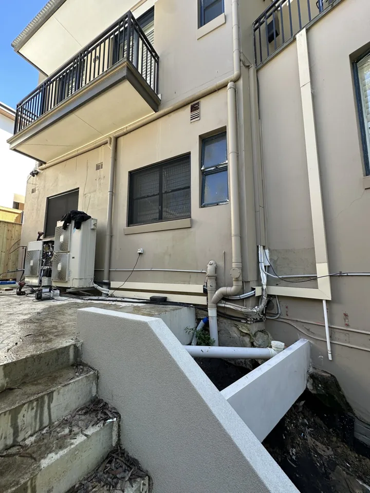Relocated air conditioning system and new pipework beside a multi-level residential building; lower pipework was pre-existing